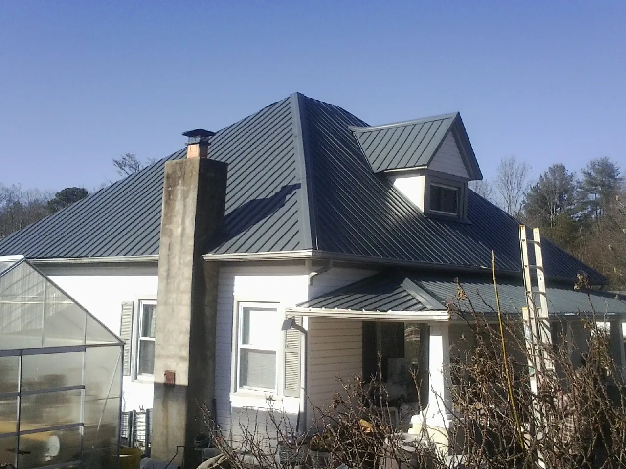 Dark blue standing seam metal roof on a white farmhouse with dormer — Slate & Tile Roof Repair by Roofing Brothers in River Rouge