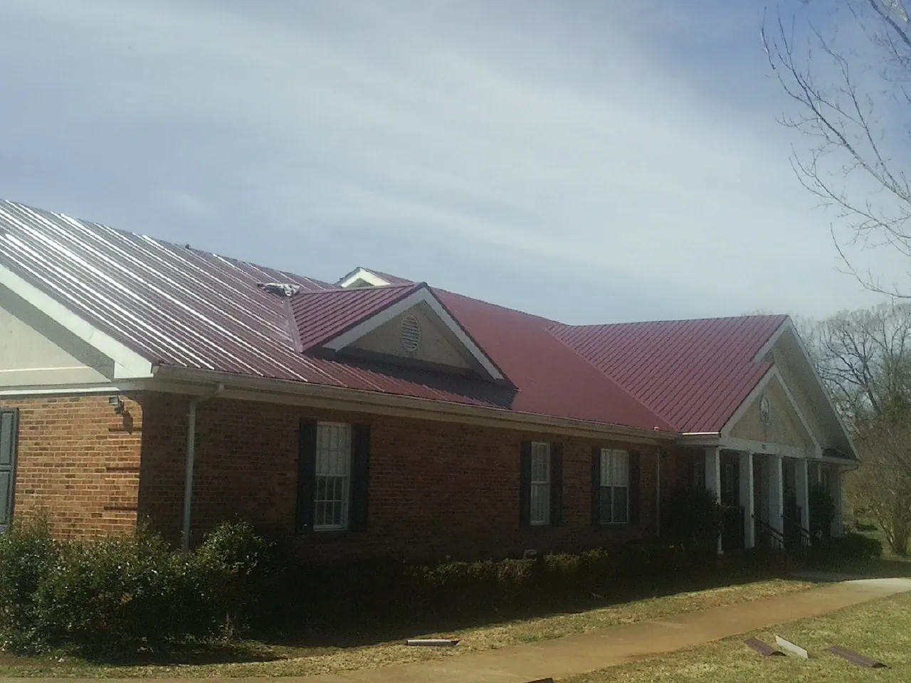 Red metal roof with gabled entries on a long brick building, from a Hail Damage Roof Repair job in River Rouge