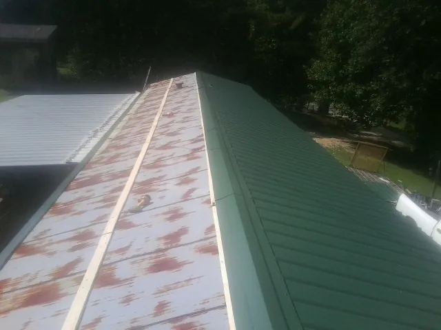 Old rusted panels beside newly installed green metal roofing — Wind Damage Roof Repair by Roofing Brothers in River Rouge