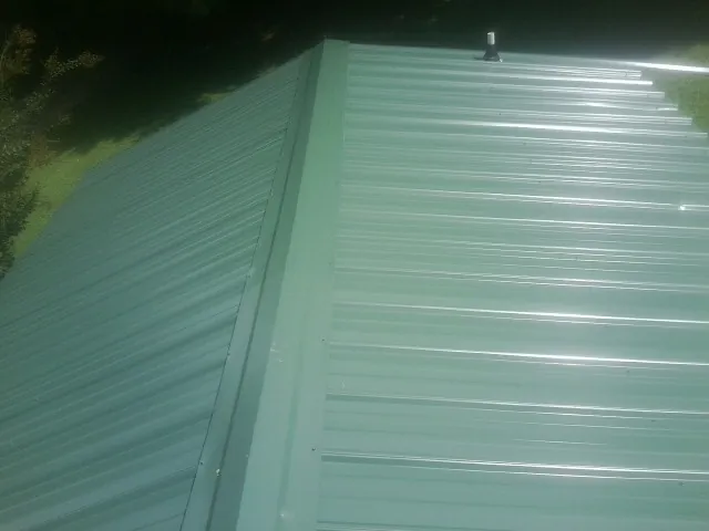 New green metal panels meeting at the ridge of a roof — Flat Roof Repair work by our crew in River Rouge