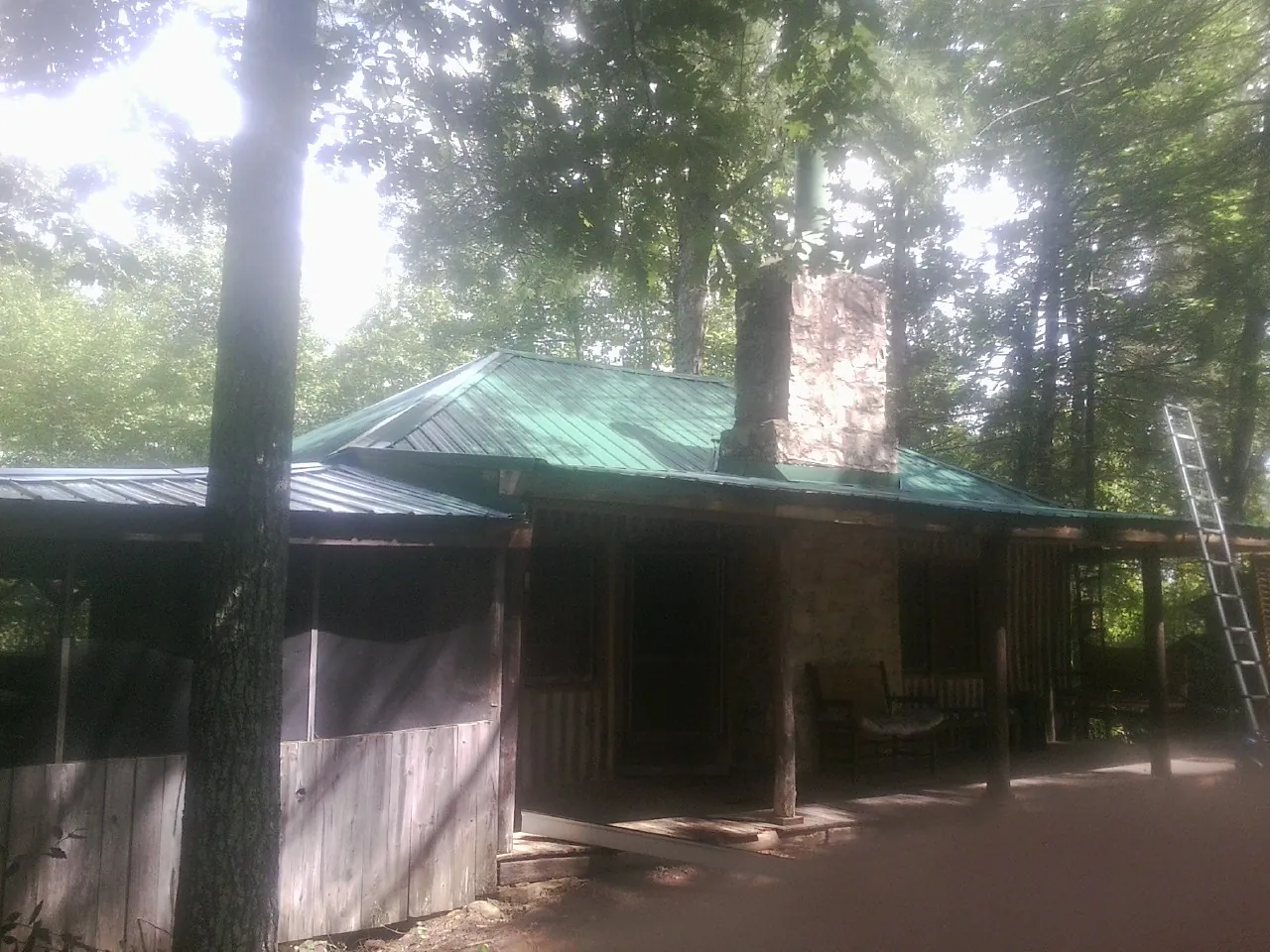 Green metal roof and stone chimney above a log cabin porch in River Rouge