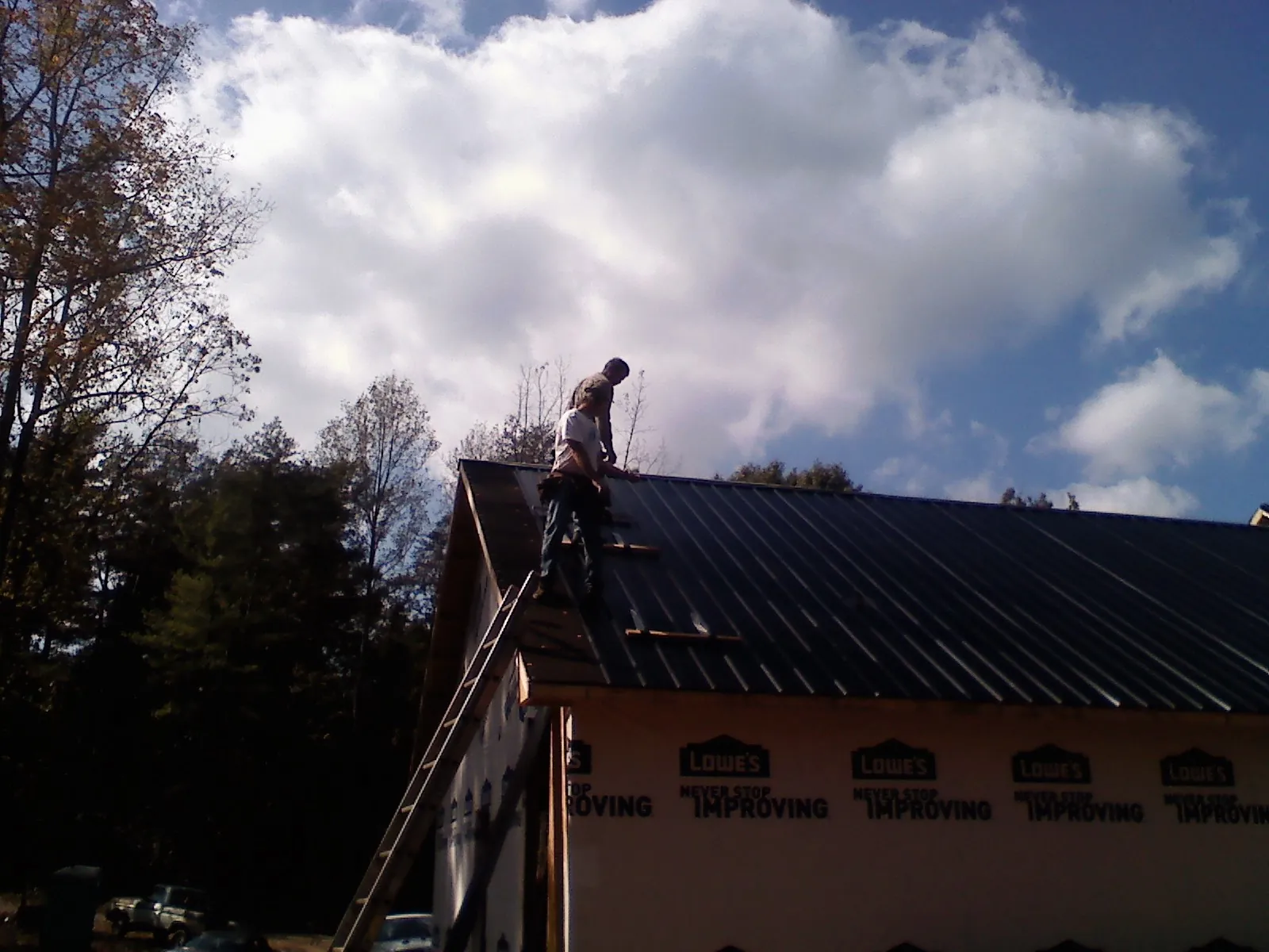 Roofer fastening dark metal panels high against a cloudy sky, from a Roof Inspection job in River Rouge