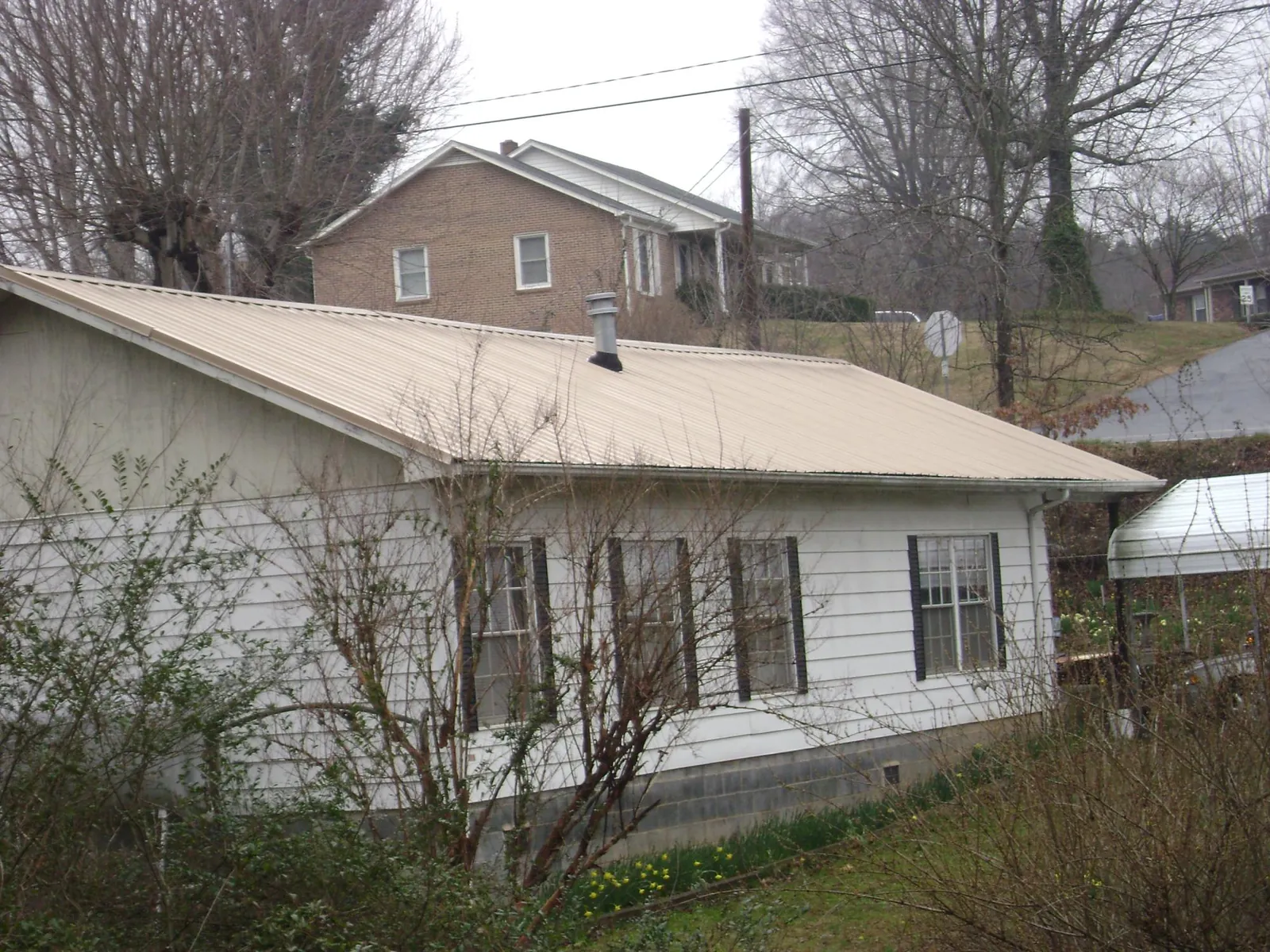 Tan metal roof on a white sided house set into a hillside — Commercial Roofing by Roofing Brothers in River Rouge
